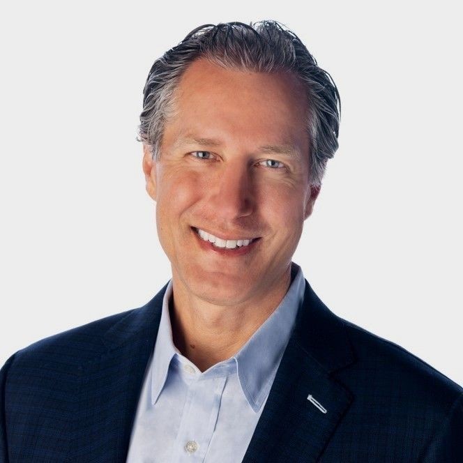 Man wearing a dark business suit and light blue dress shirt with a white background.